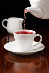 Tea is poured from the teapot into a cup. Porcelain teaware. Side view. Selective focus.
