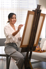 Pleasant millennial woman painting picture on canvas with oil paints in home studio. Leisure activity, creative hobby and art concept