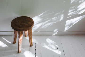 Wooden stool near the white wall, rustic interior details. - obrazy, fototapety, plakaty