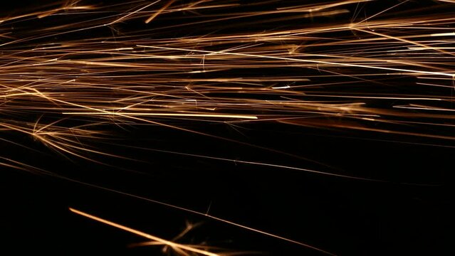 Bright sparks on a black background. Sparks of fire fly and fall. Cut metal. Metallic fireworks. A spark from a cutting wheel.