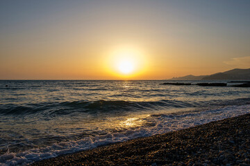 Gorgeous sea sunset landscape. MIrror reflection of dawn on wet pebble. Golden sunlight over sea waves.