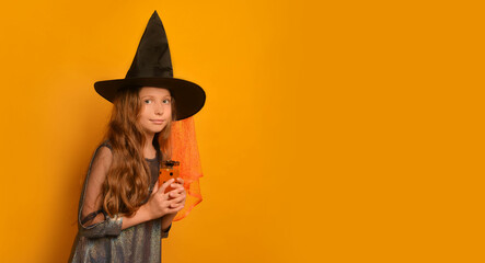 Witch kid girl holding festive juice glass or lemonade glass, leaning forward and looking at camera on yellow background with copy space for text.

Girl celebrating Halloween in wizard witch costume.
