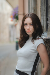 Beautiful Ukrainian girl with red hair, blue eyes and freckles in a grey summer dress leaning with his back against a wall in a cobbled street with street lamps in the old town, vertical