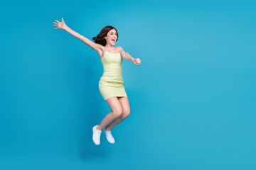 Fototapeta na wymiar Full length photo of excited funky lady wear green outfit jumping high arms sides looking empty space isolated blue color background