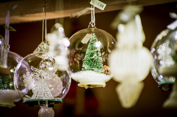 Advent Bazaar Stalls with glass, wooden, ceramic christmas souvenirs in a shop. Close up of festive decorations for tree in winter street night market during new year's holiday. Illuminated fair kiosk