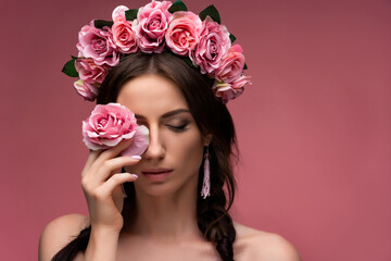 A wreath of pink roses is a beautiful headdress for a girl. Portrait of an attractive young Ukrainian woman in a wreath with clean skin. Concept wedding style or beauty salon and skin care.