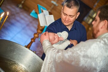 Baptism of a newborn in holy water. Bathing youth on the water. Baptism in the font. The sacrament of baptism. Child and God. Baptismal candle with holy water. Priest baptizes - obrazy, fototapety, plakaty