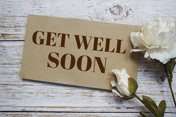 Get well soon text message on paper card with flower decoration on wooden background