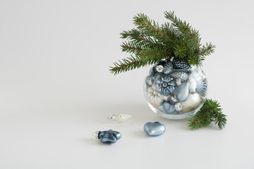 Christmas home decoration. Christmas toys and fir branches in a glass vase on a light background. Christmas and New Year background.