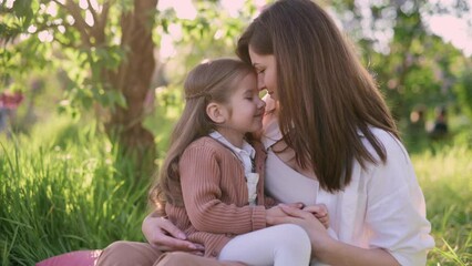 A young mother holds a cute little daughter in her arms near a flowering tree. Portrait of a four-year-old girl in the arms of a loving mother. - Powered by Adobe