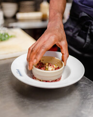 Un chef dresse un carpaccio avec un emporte pièces dans les cuisines d'un restaurant