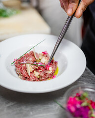 Un chef dépose une fleur rose avec des pincettes sur un carpaccio dans un restaurant
