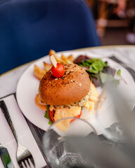 Un hamburger coloré dégoulinant de fromage dans un restaurant avec une tomate cerise en décoration