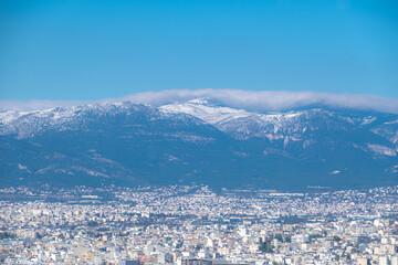 Part of Athens city during winter with blue sky and mountain peak with snow at the background.