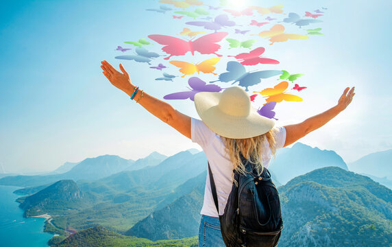 Happy celebrating winning success woman at sunset or sunrise standing elated with arms raised up above her head in celebration of having reached mountain top summit goal during hiking travel trek.
