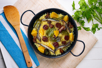 Migas with chorizo, sardines, bacon and green peppers cooked in a black paella. Typical Spanish tapa recipe.
