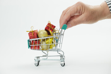 Hand woman rolls full of Christmas gifts and Christmas decorations little shopping cart. The concept of Christmas sales, buying gifts for the winter holidays.