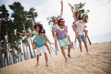 Full size portrait of overjoyed carefree people have fun piggyback ride enjoy walking sand beach...