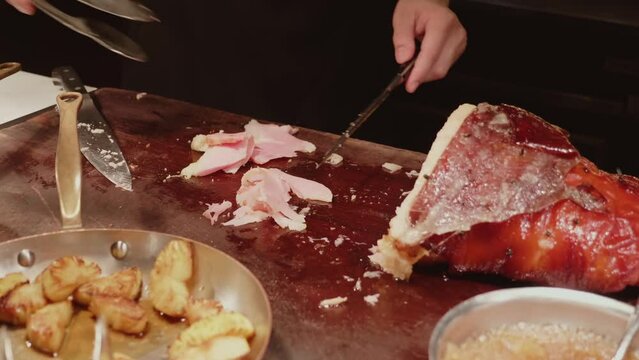 Chef slices roasted pork ham from the smoked leg in luxury restaurant