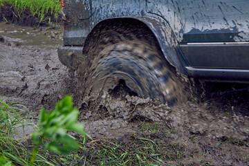 Fototapeta na wymiar Blue offroader has stalled in the mud during an off-road race, the wheels are prepares on the slush. Blurry photo of a moving SUV. The wheel of the off road rotates in a puddle of mud