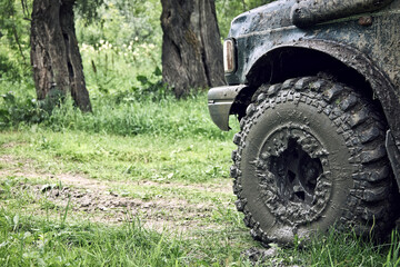 Fototapeta premium Dirty SUV is standing on the lawn after an off-road race, covered in slush. A beautiful photo of nature and an SUV in a beautiful meadow. Side view of the lowered wheel of an extreme car