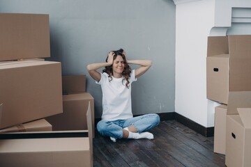 Tired stressed girl holding her head sitting with boxes having problem with relocation on moving day