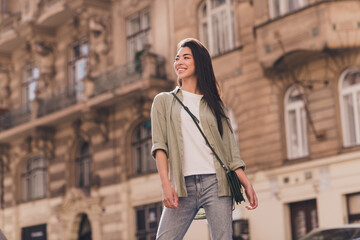 Photo of positive shiny young asian woman wear khaki shirt enjoying summer sunshine walking outside urban city street