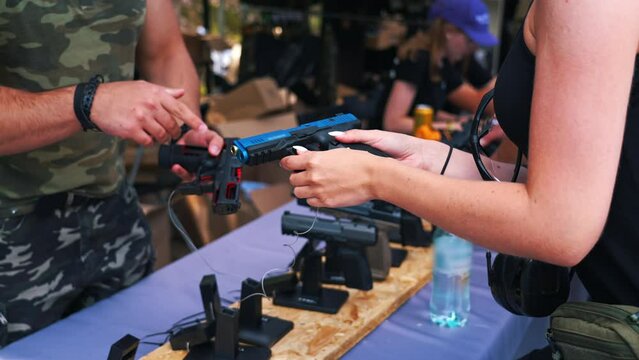 Two unrecognizable caucasian people in moro-patterned clothing talking over a black gun and compering weapons. Gunsmithing concept. . High quality 4k footage