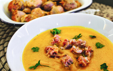 Pumpkin soup in a white ceramic bowl with bits of sausage and fresh coriander leaves sprinkled on top