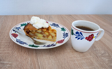 Traditional Dutch apple pie with whipped cream and a cup of coffee. Ceramics are in hand painted farmer's pattern ('boerenbont') on a wooden table.