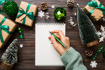 Woman writing Christmas to do list on notebook on colored background with xmas decorations