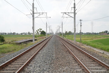 Rocky train rail in near the train station at noon with green paddy field scenery

