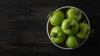 white cup full of tomatoes, freshly harvested green berries on a rustic black wooden table top, taken from above with copy space