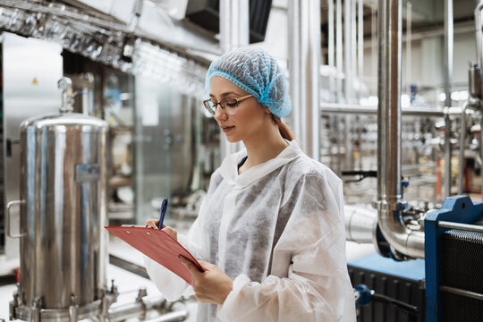 Female Worker In Protective Workwear Working In Medical Supplies Research And Production Factory And Checking Canisters Of Distilled Water Before Shipment. Inspection Quality Control.