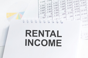 Rental income inscription on a notebook on a table with reports and diagrams, a business concept