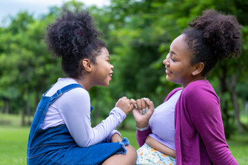 African American mother is giving pinky promise to her young daughter while having a summer picnic...