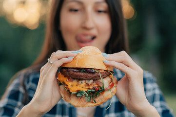 Young attractive hungry woman bites a big hamburger outdoor. Close up.