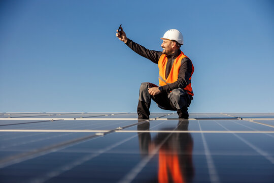 A worker is taking selfie with solar panels on the rooftop and smiling at the phone.