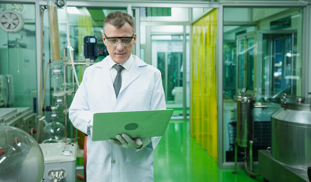 Caucasian male scientist in lab uniform is holding and using computer to search for information about cannabis and CBD extraction. Expert marijuana researcher concentrate on working in laboratory.
