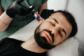 Beauty treatments for a stylish young man with a beard. Beautician makes beauty injections in a man's face