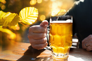 Sunny autumn day in the beer garden. Guest with fresh filled beer mug in the hand and golden autumn leaves in the background. - obrazy, fototapety, plakaty