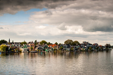 vecindario de casas tradicionales al borde del canal con reflejos en el agua y cielo con nubes en un pueblo rural de holanda, países bajos