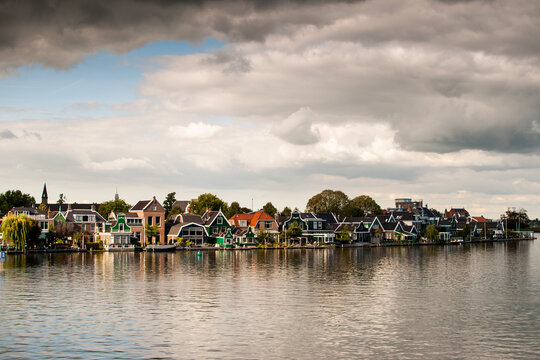 vecindario de casas tradicionales al borde del canal con reflejos en el agua y cielo con nubes en un pueblo rural de holanda, pa&iacute;ses bajos