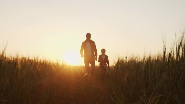 Farmer and his son in front of a sunset agricultural landscape. Man and a boy in a countryside field. Fatherhood, country life, farming and country lifestyle concept.