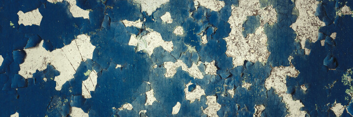 Peeling paint on the wall. Panorama of a concrete wall with old cracked flaking paint. Weathered rough painted surface with patterns of cracks and peeling. Panoramic texture for background and design.