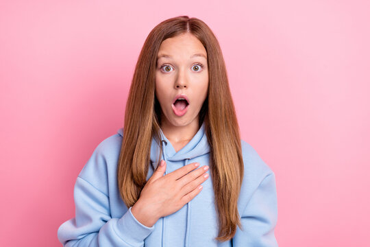 Closeup photo of young funny excited shocked little schoolgirl wear blue hoodie touch chest reaction open mouth grimace isolated on pink color background