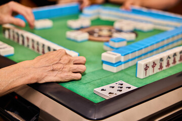 Fototapeta premium Elderly people playing mahjong, indoor gamble activity at home during spring festival.