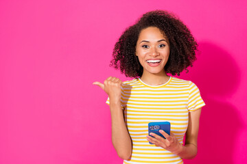 Photo of stunning young lady hold telephone point empty space dressed stylish yellow striped look isolated on shine pink color background
