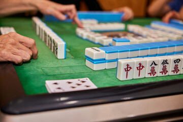 Fototapeta premium Elderly people playing mahjong, indoor gamble activity at home during spring festival.