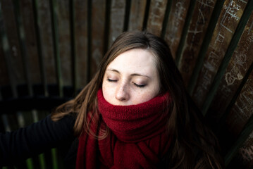 Close-up portrait of a thirty year old attractive white girl wearing a red winter scarf, eyes closed